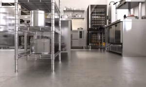 Concrete floor of commercial, professional bakery kitchen, stainless steel convection, bread bun in deck oven, freezer, refrigerator, kneading machine, cabinet, ingredient on table