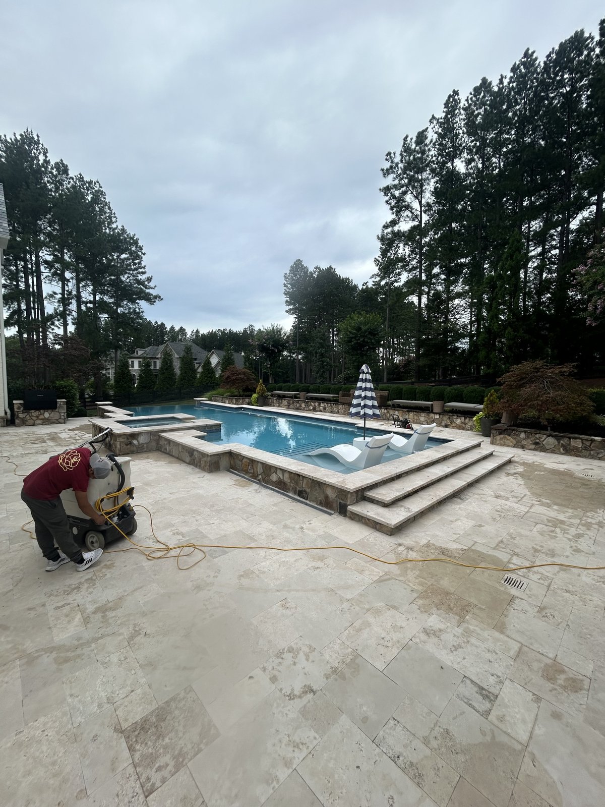 Rose Restoration technician honing large travertine pool deck at luxury residential property