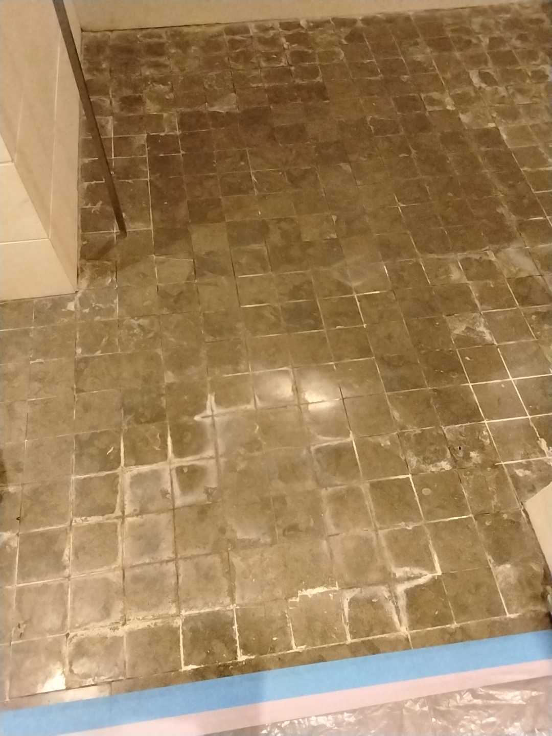 Soiled natural stone mosaic bathroom floor with darkened tiles and mineral haze across the grout before restoration