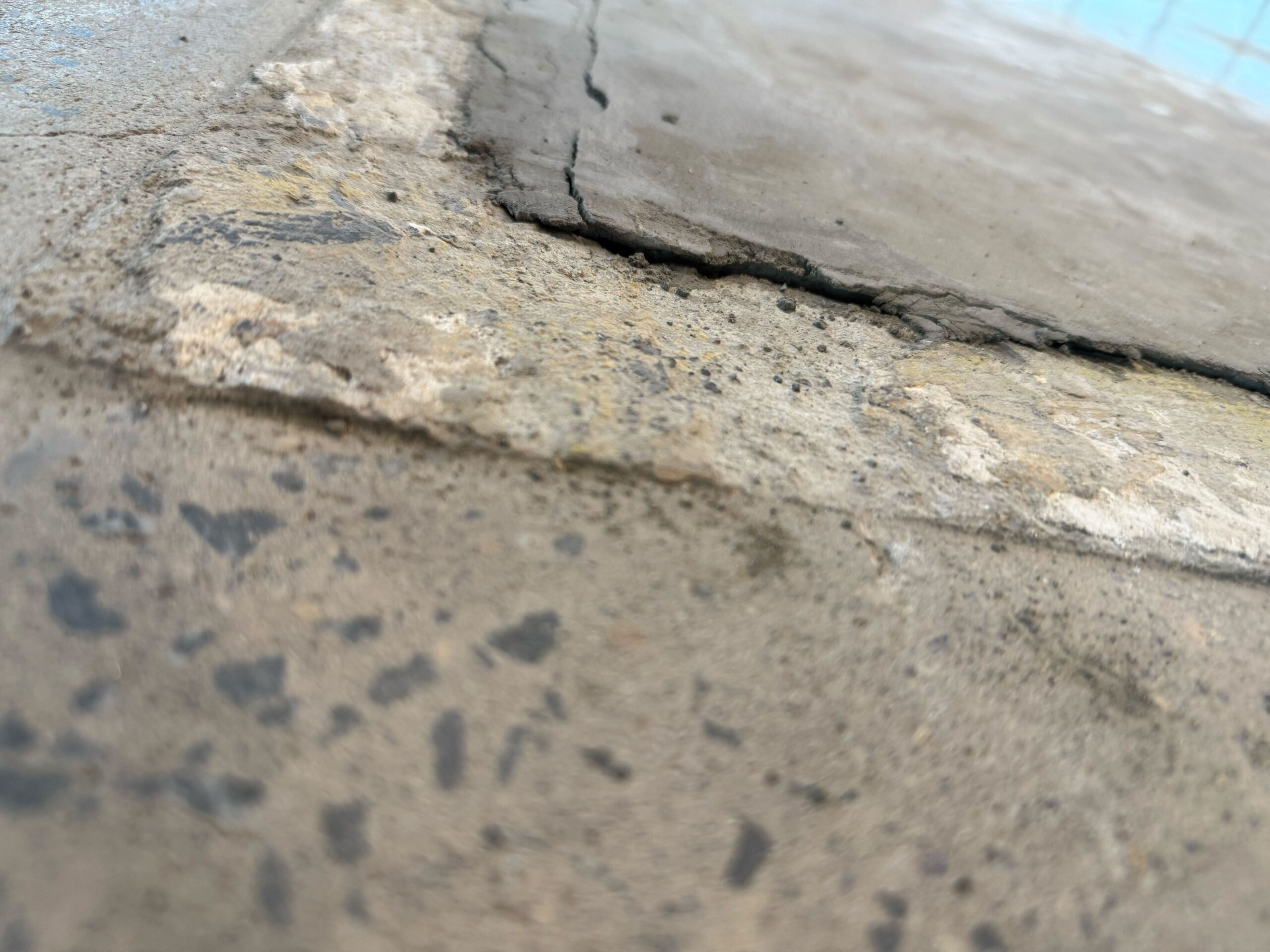 Spalled and delaminated concrete edge at a failed joint beside a pool, with aggregate exposed