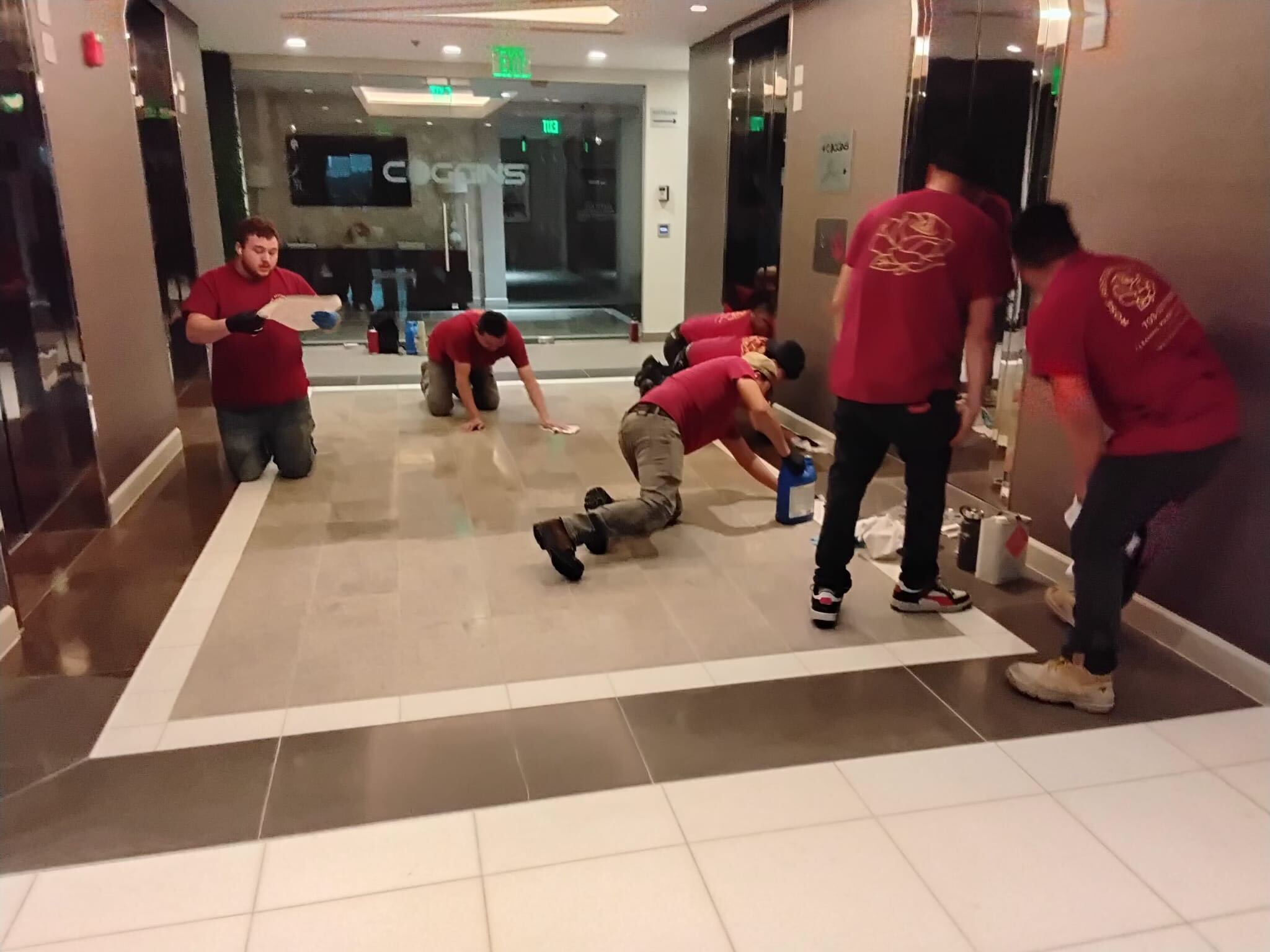 Rose Restoration crew in branded shirts honing and polishing a marble corridor floor in a commercial lobby