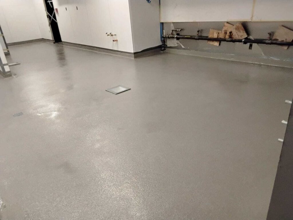 Gray epoxy floor coating in commercial kitchen with floor drain showing smooth seamless finish by Rose Restoration
