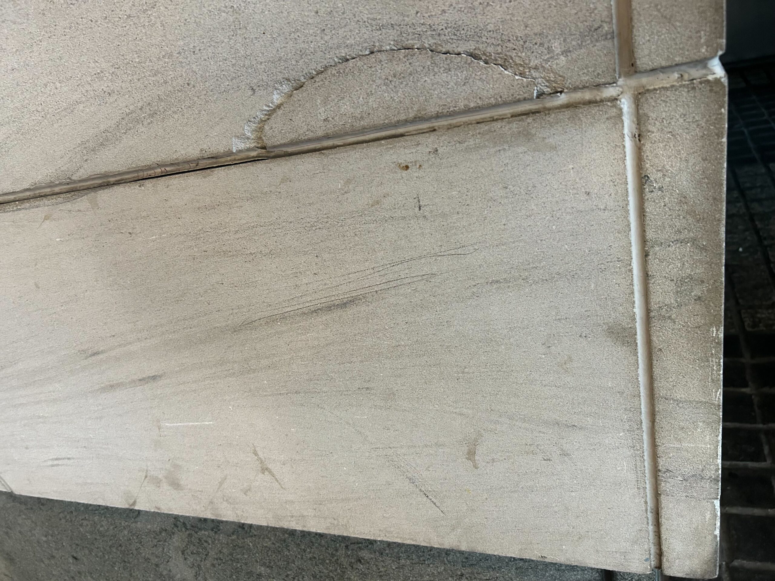 Crescent-shaped chip loss along the jointed edge of a light stone panel, with surface soiling