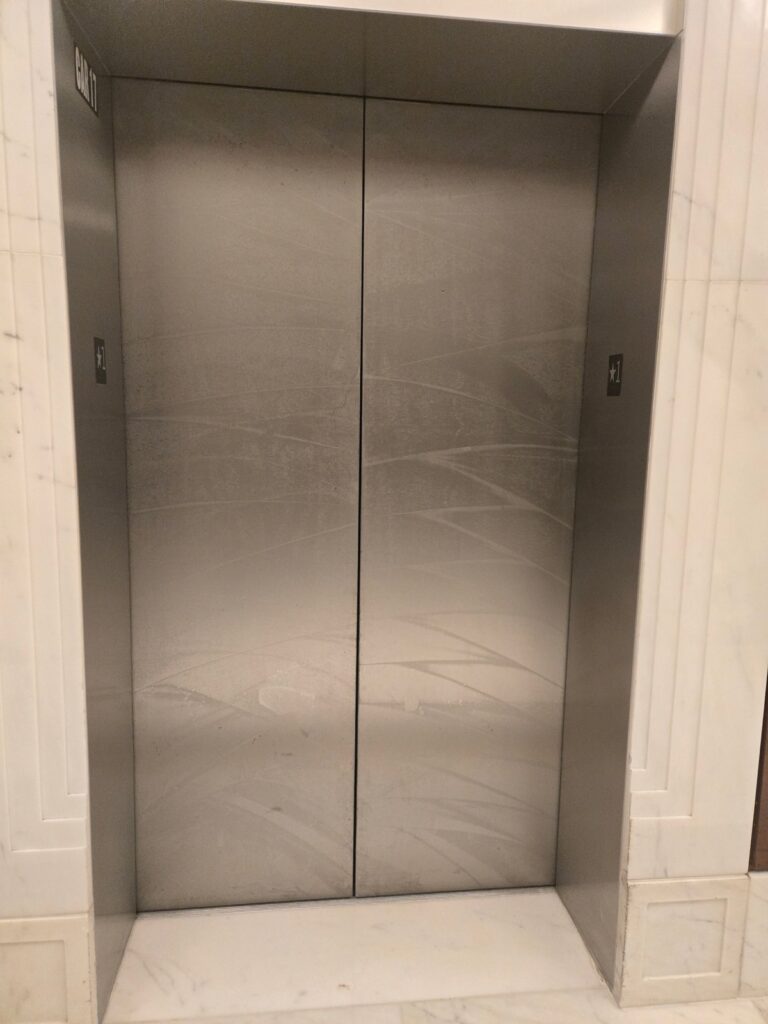 Commercial elevator doors with surround before Rose Restoration metal and stone restoration