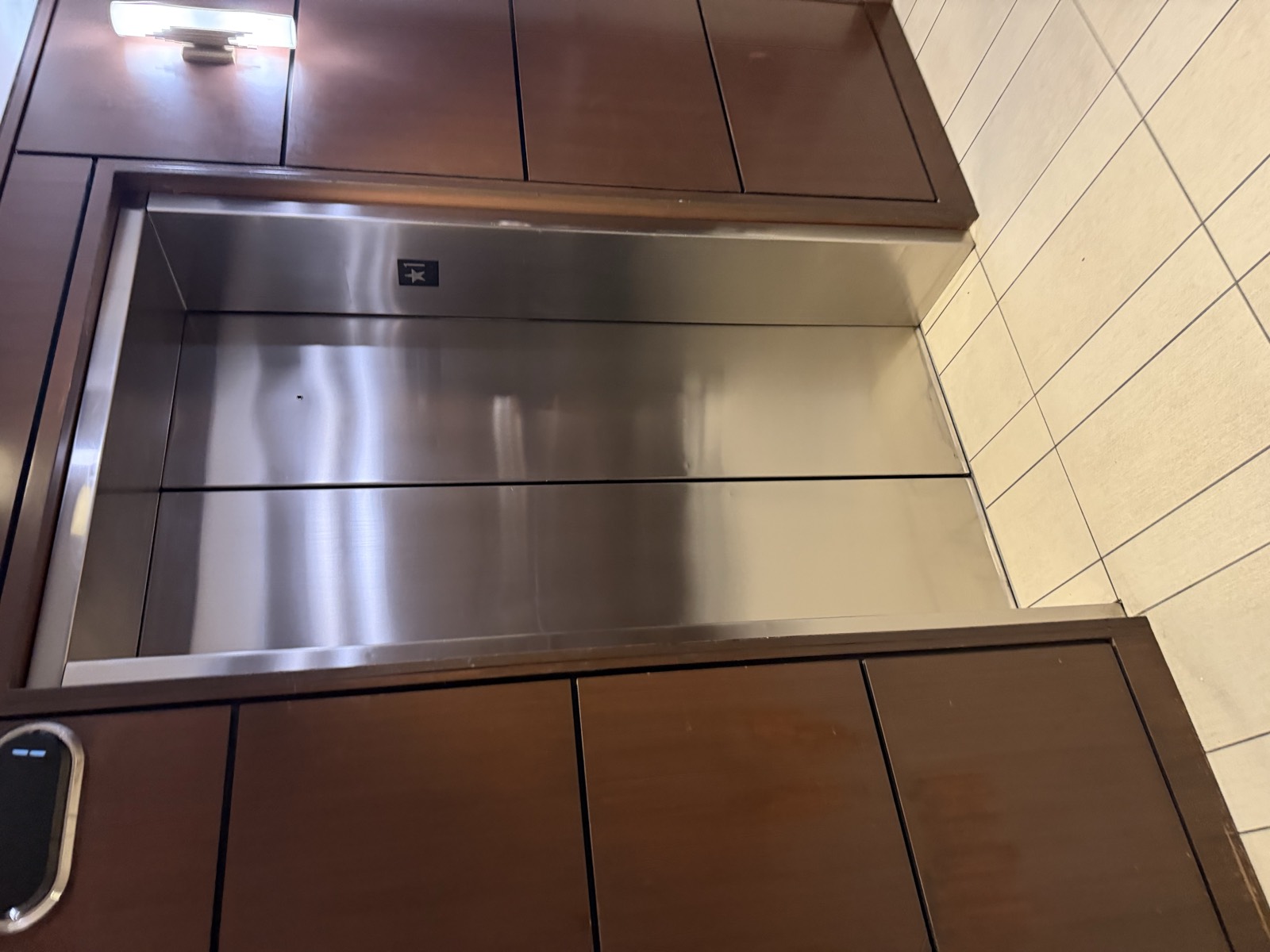 Corner detail inside a restored elevator cab where bronze wall panels meet a stainless steel handrail