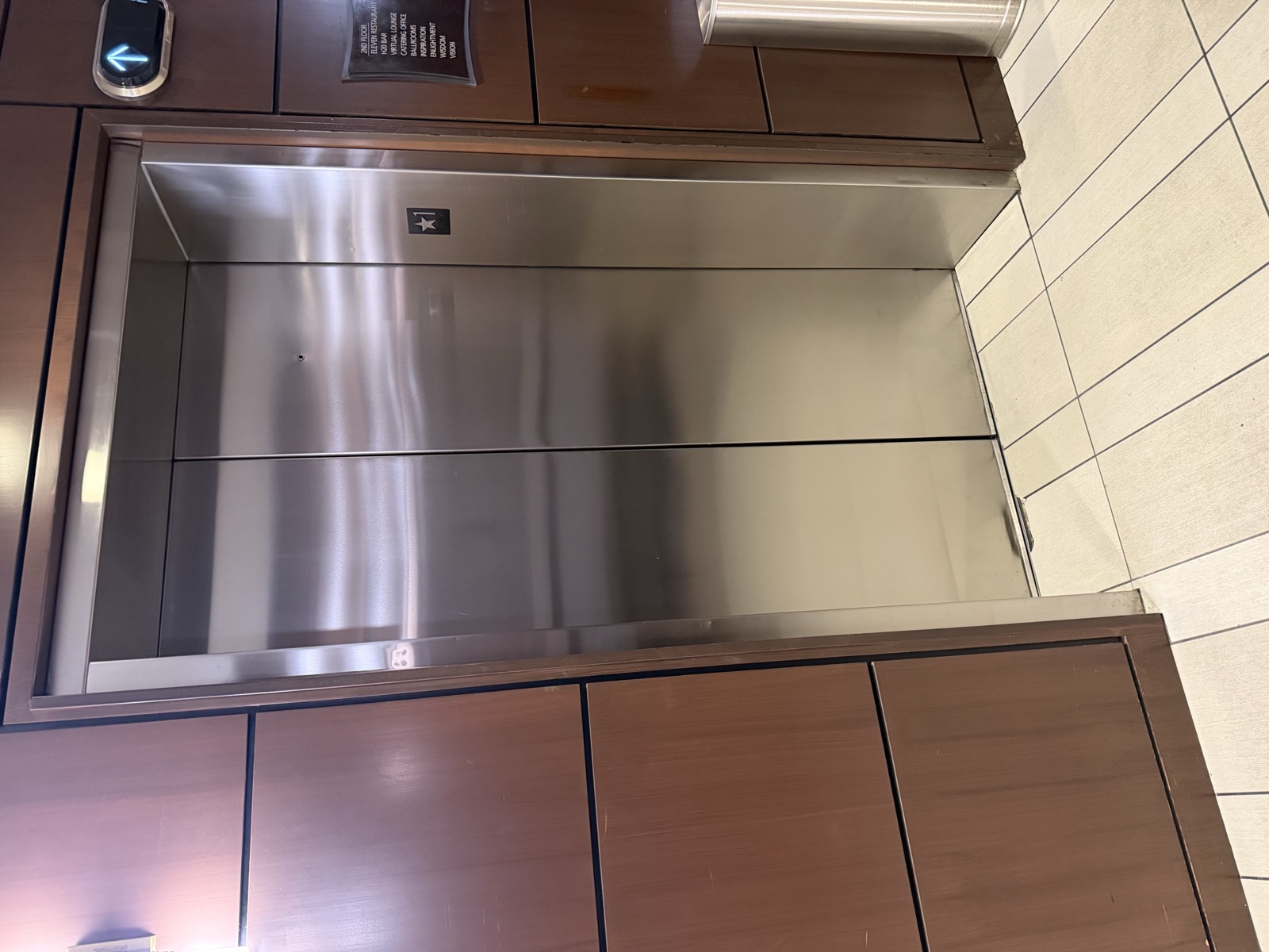 Restored elevator cab interior with dark bronze wall panels, stainless steel handrail and stone base