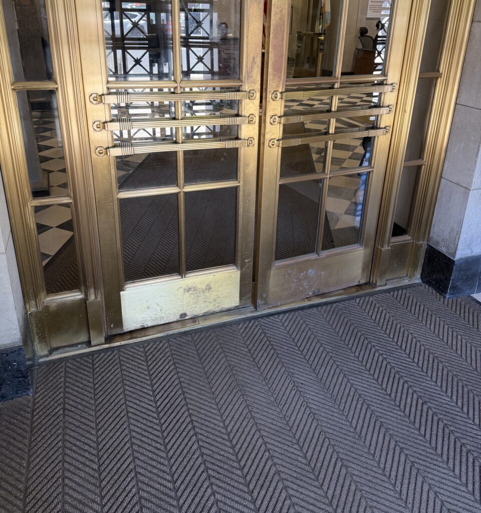 Restored Art Deco brass entrance doors with a geometric grille in a historic building lobby