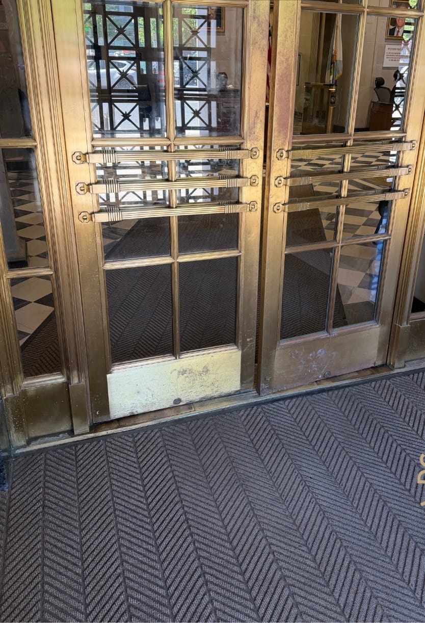 Tarnished brass entrance doors before restoration, the finish dulled and darkened and the kick panel oxidised