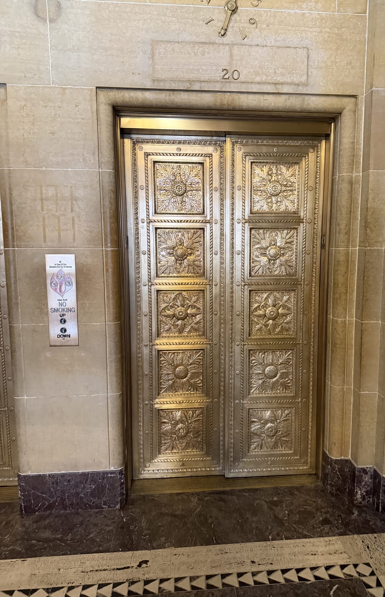Ornate cast bronze elevator doors with foliate rosette panels in a limestone surround
