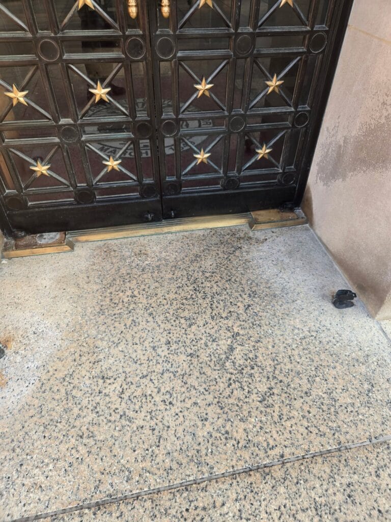 Dark metal doors with a star grille above a terrazzo floor