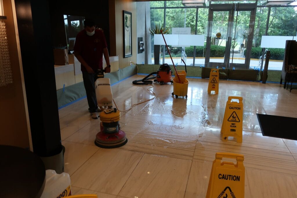 Floor machine cleaning an office lobby with warning signs out
