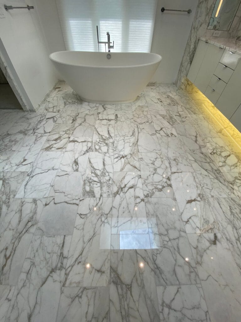 White marble bathroom floor with bold grey veining and a freestanding tub