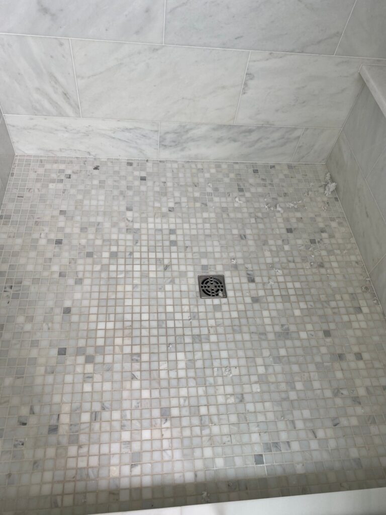 White marble shower with a mosaic floor and large marble wall panels