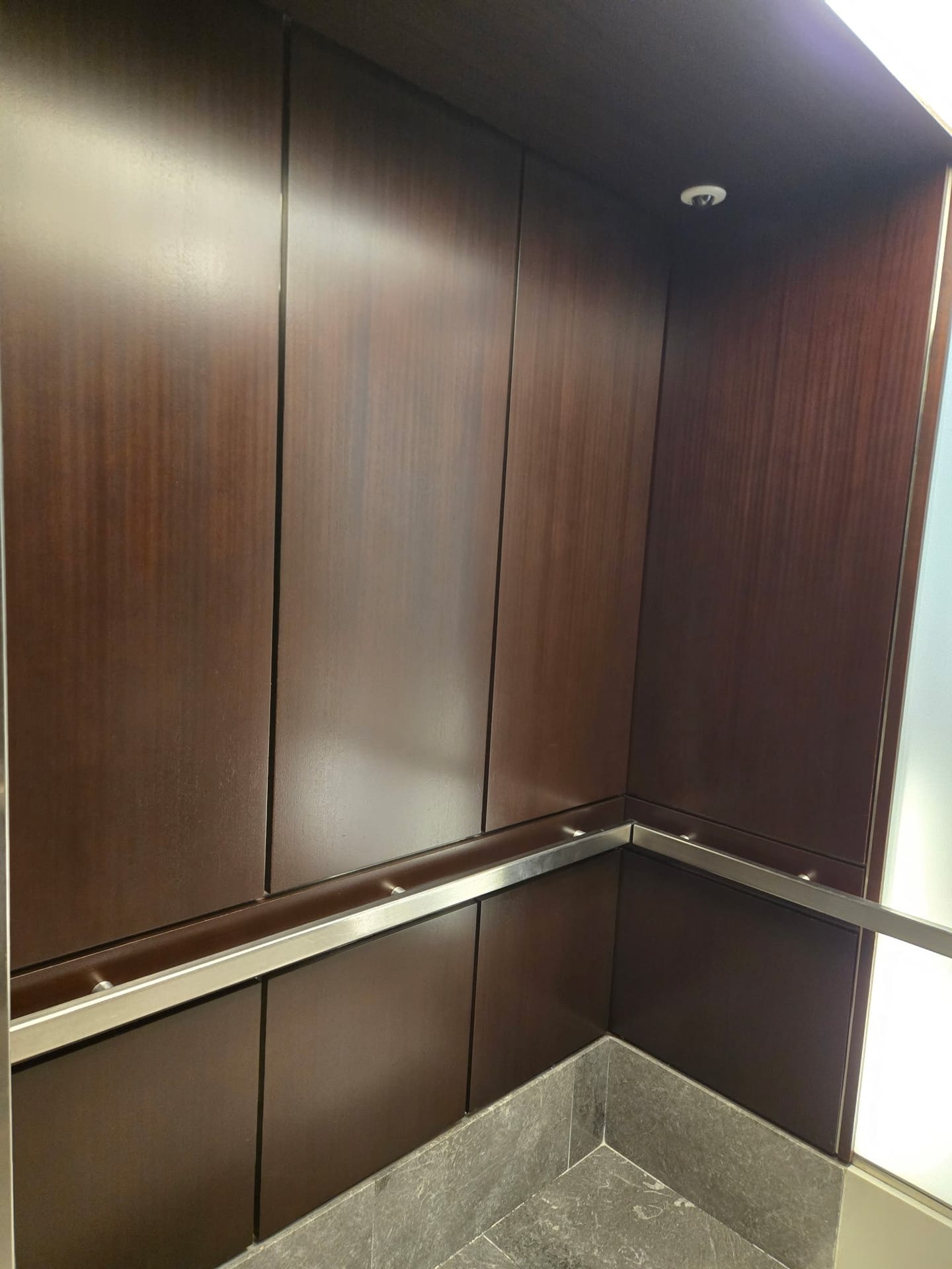 Corner of a wood-panelled elevator cab after refinishing, showing grain and a level sheen