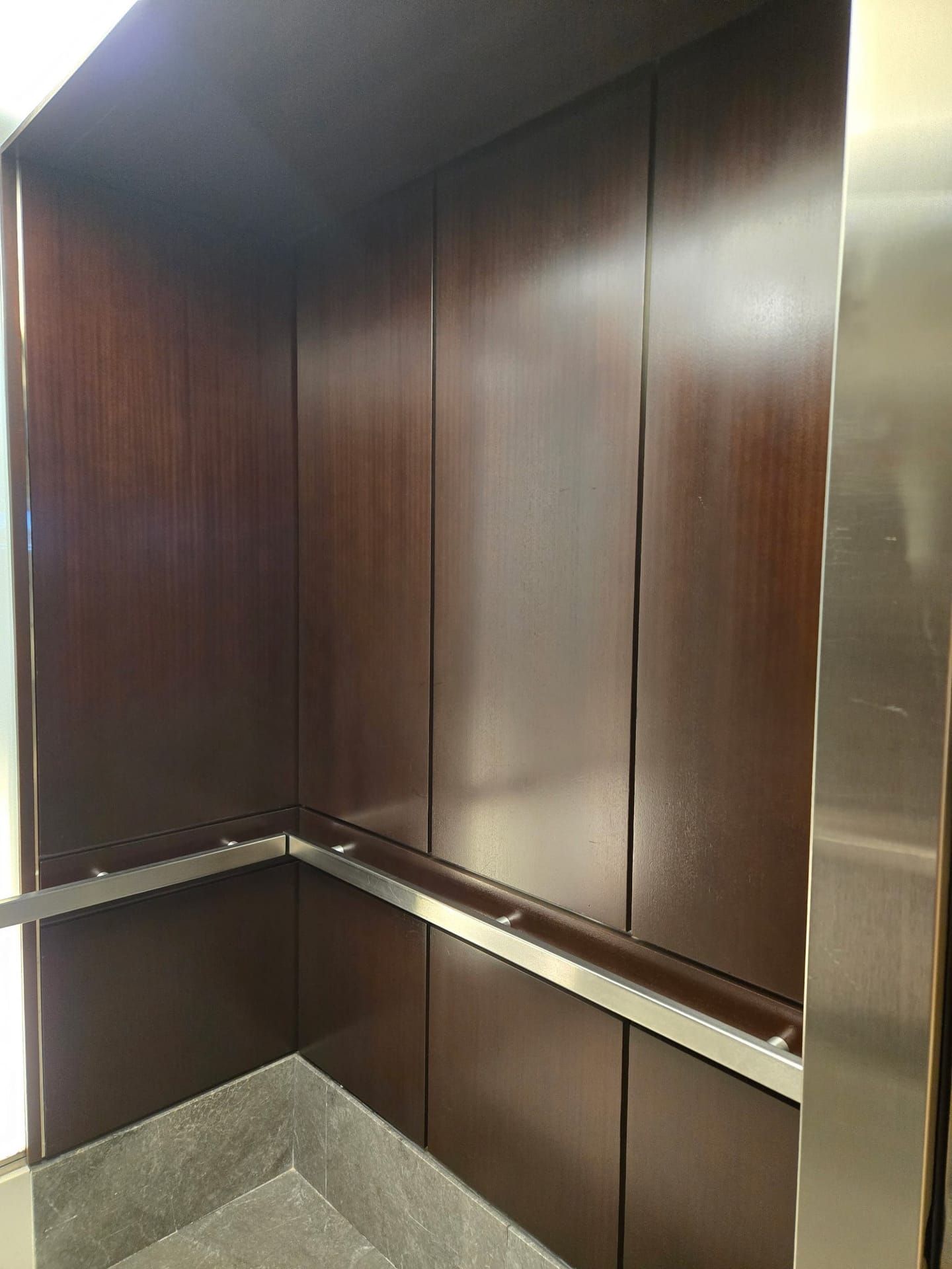 Wood elevator cab panelling restored in place, with stainless trim and a stone kick panel