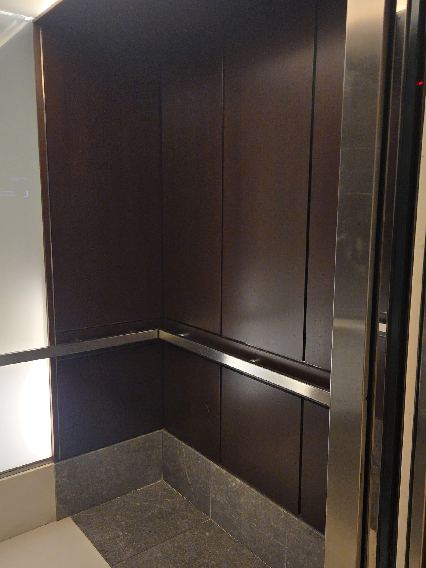 Wood-panelled elevator cab with a polished stainless handrail after restoration