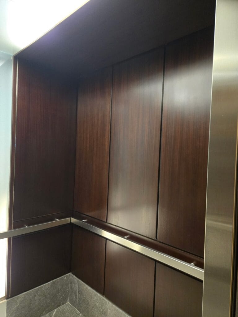 Dark wood elevator cab panelling refinished to an even sheen, with a stainless handrail