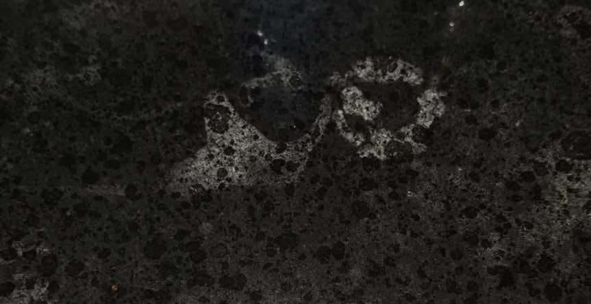 Close-up of cloudy, dull patches on a dark granite countertop before restoration