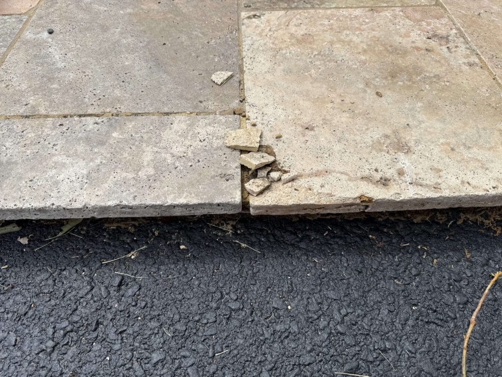 Loose and chipped patio edge stones beside a driveway in Chantilly, VA before repair