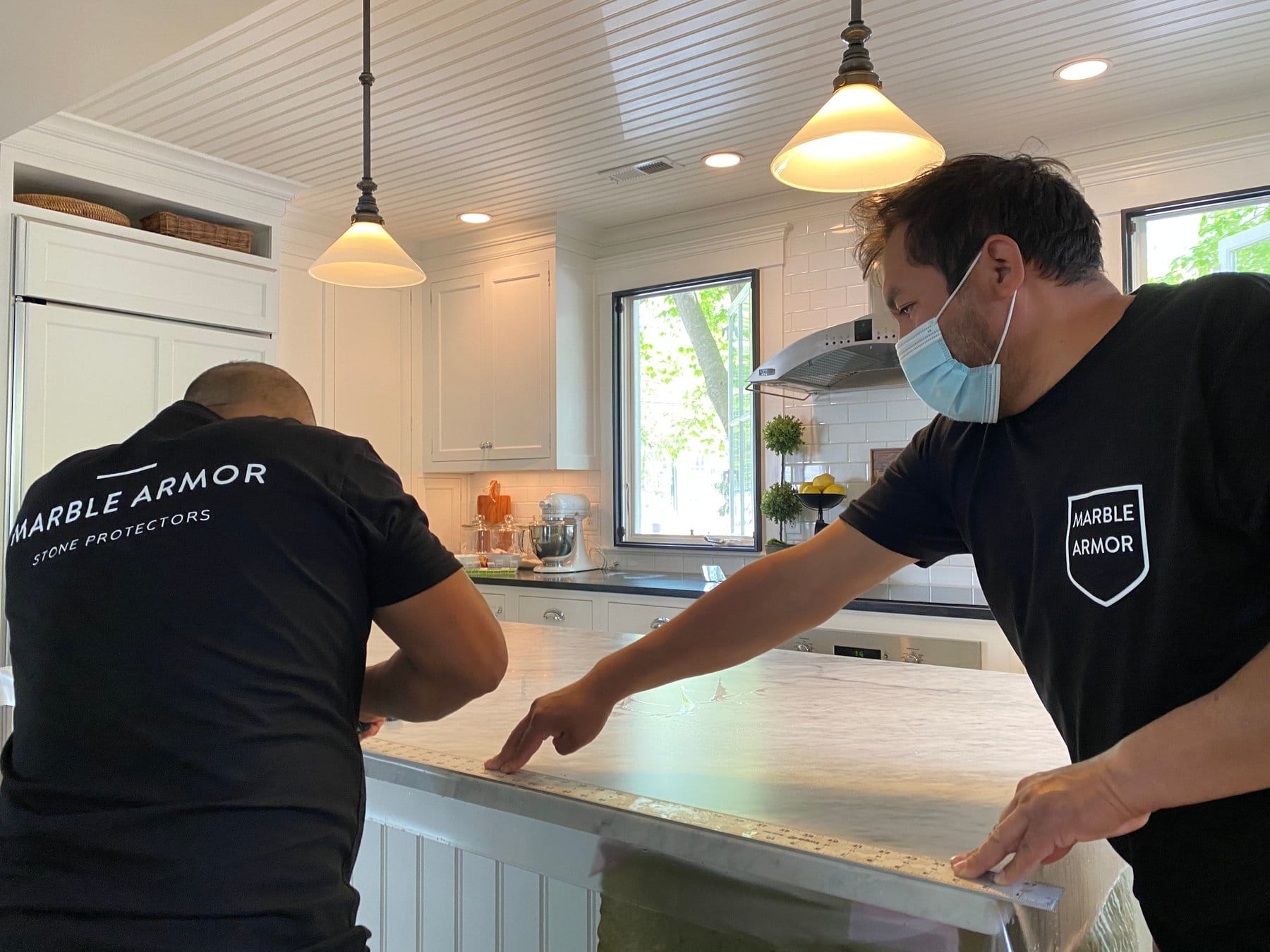 Two installers smoothing Marble Armor film on a large marble island