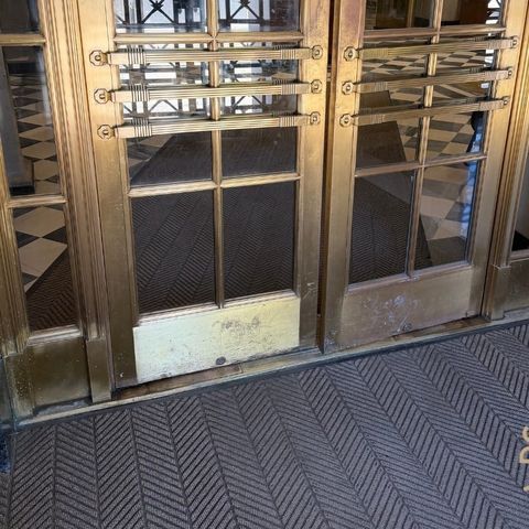 Tarnished brass entrance doors with oxidized, patchy finish and a grey kick panel before restoration by Rose Restoration